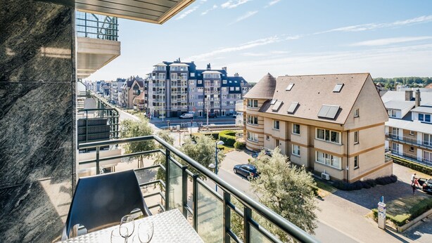 A balcony with a table and chairs, overlooking a residential area with modern buildings and a clear sky. - Apartment in Koksijde Near the Sea (Koksijde)