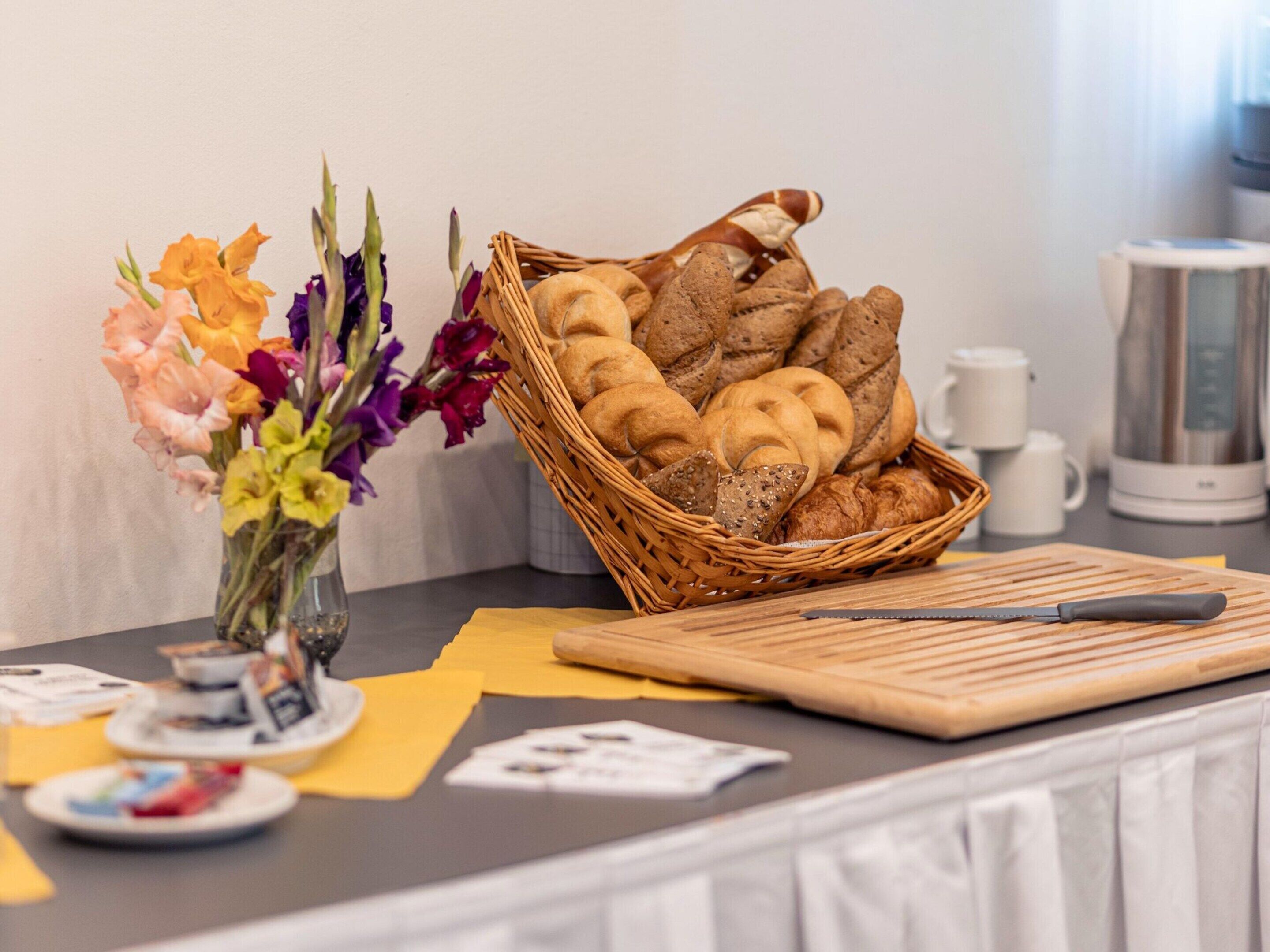Uma bancada de cozinha com uma cesta de pão, uma faca e um vaso de flores.