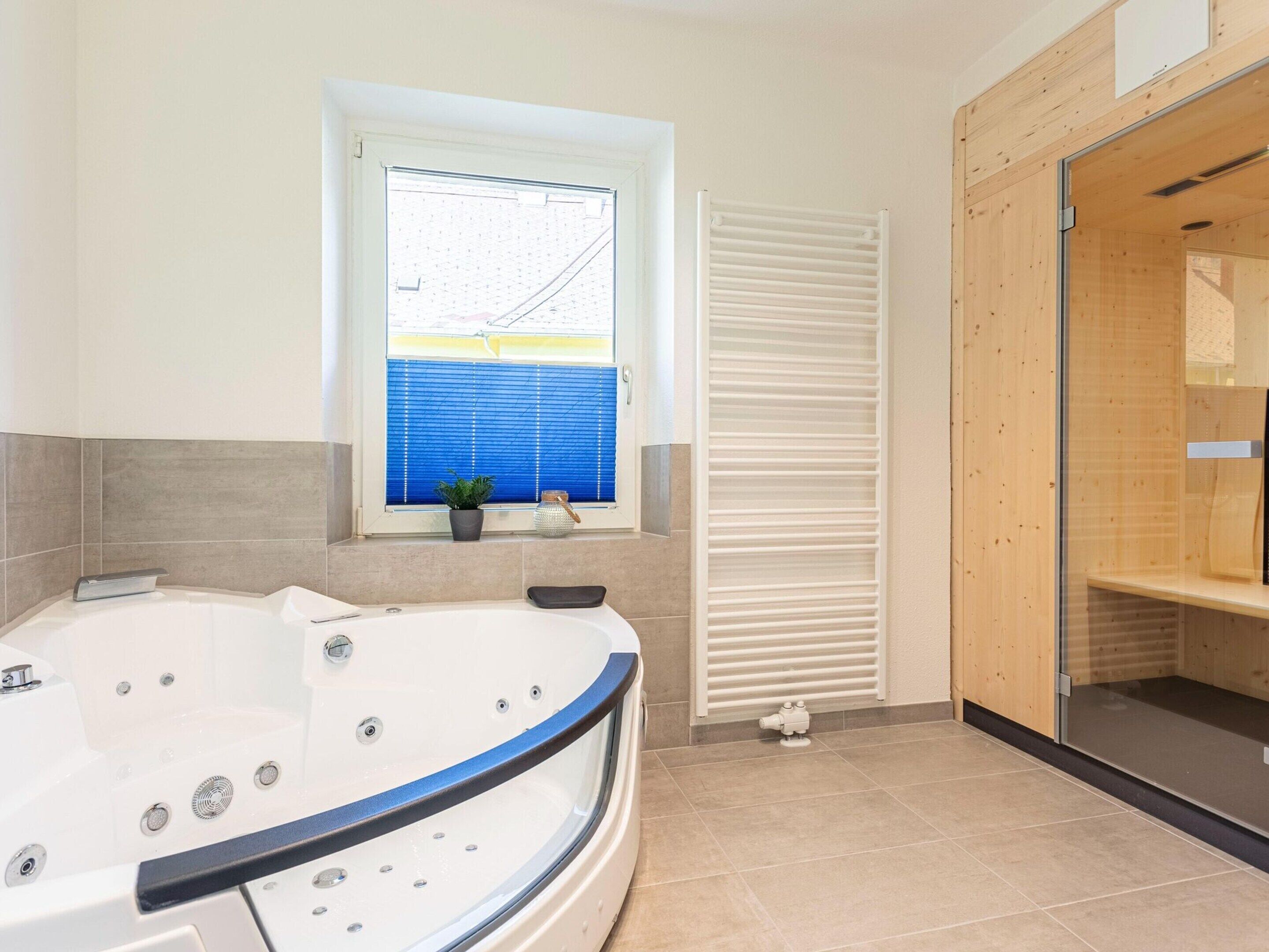A modern bathroom with a freestanding bathtub, a window with blinds, and a wooden shower enclosure.