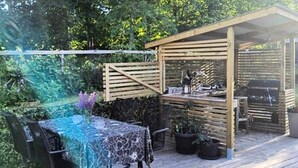 Une terrasse extérieure agrémentée d’une pergola en bois, d’une table avec des chaises et de plantes en pot.