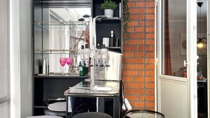 A compact kitchen with a modern design, featuring a built-in stove, a glass shelf with kitchenware, and a brick accent wall. - 8 Person Holiday Home in Hallekis (Hallekis)
