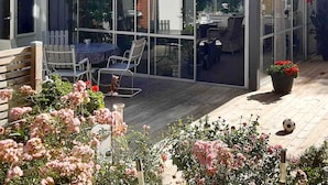 Un patio couvert avec une structure en verre, des meubles d’extérieur et une terrasse en bois.