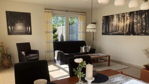 Uma sala de estar com um sofá preto, uma mesa de centro e uma mesa de jantar com um vaso de flores.
