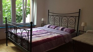A bedroom with a metal bed frame, a window with a view of greenery, and a bedside table with a lamp. - Gezellig Huisje (Zeltingen-Rachtig)