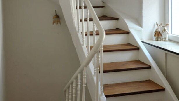 A white staircase with wooden steps and white balusters, leading to a landing with a window and a small decorative item on the sill. - Gezellig Huisje (Zeltingen-Rachtig)