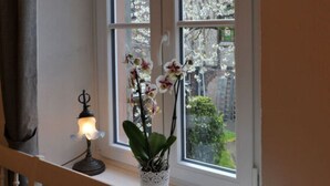 A window with a white frame, a potted orchid, and a small table lamp. - Gezellig Huisje (Zeltingen-Rachtig)