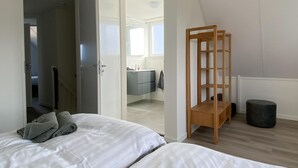 Een moderne slaapkamer met twee bedden, een houten schapenkast en uitzicht op een andere kamer.