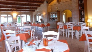 Ein Restaurant mit mehreren Tischen, weißen Stühlen und orangefarbenen Tischdecken.