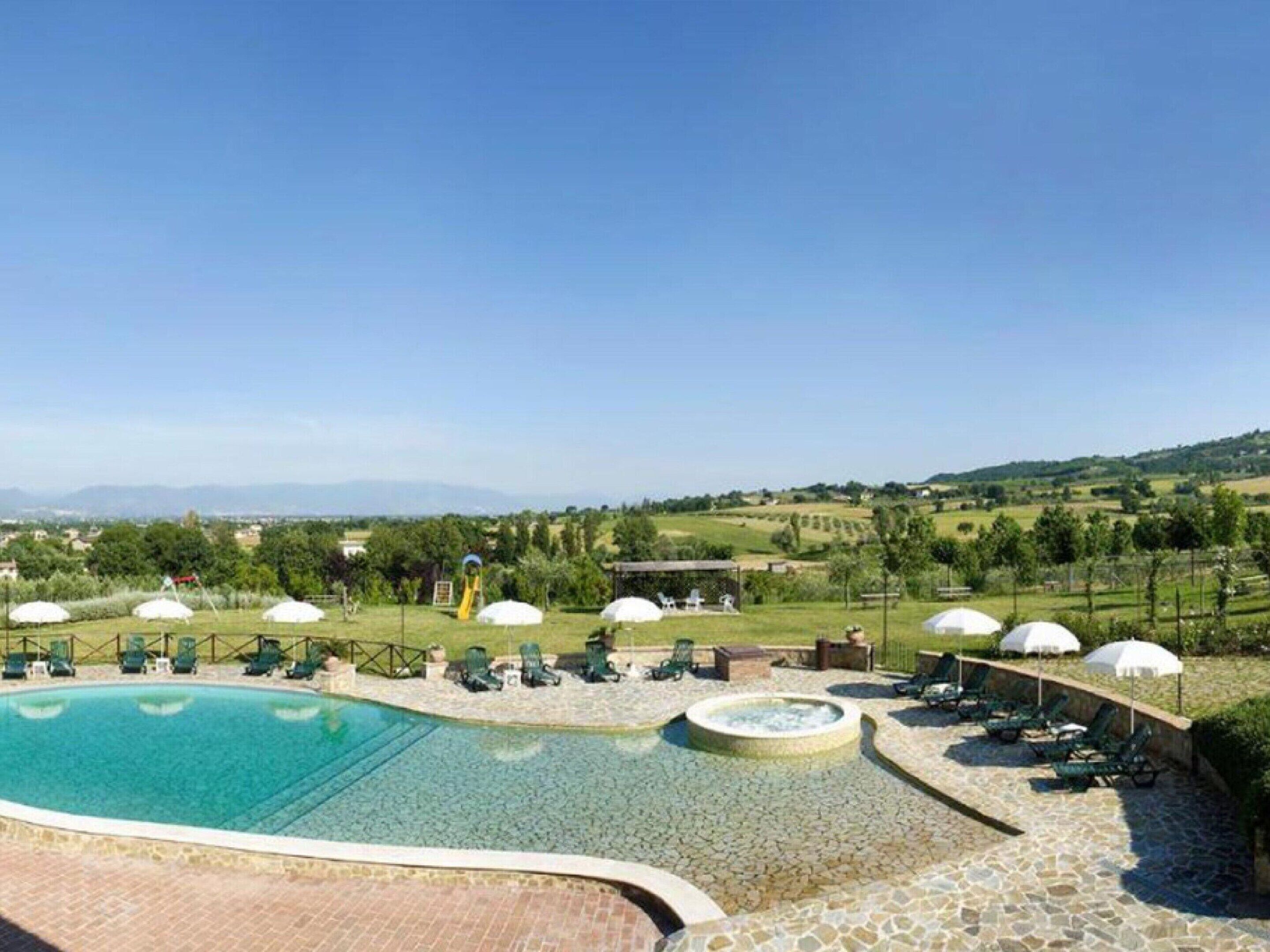 A pool area with lounge chairs and umbrellas, surrounded by yurts and a scenic view of hills and fields.