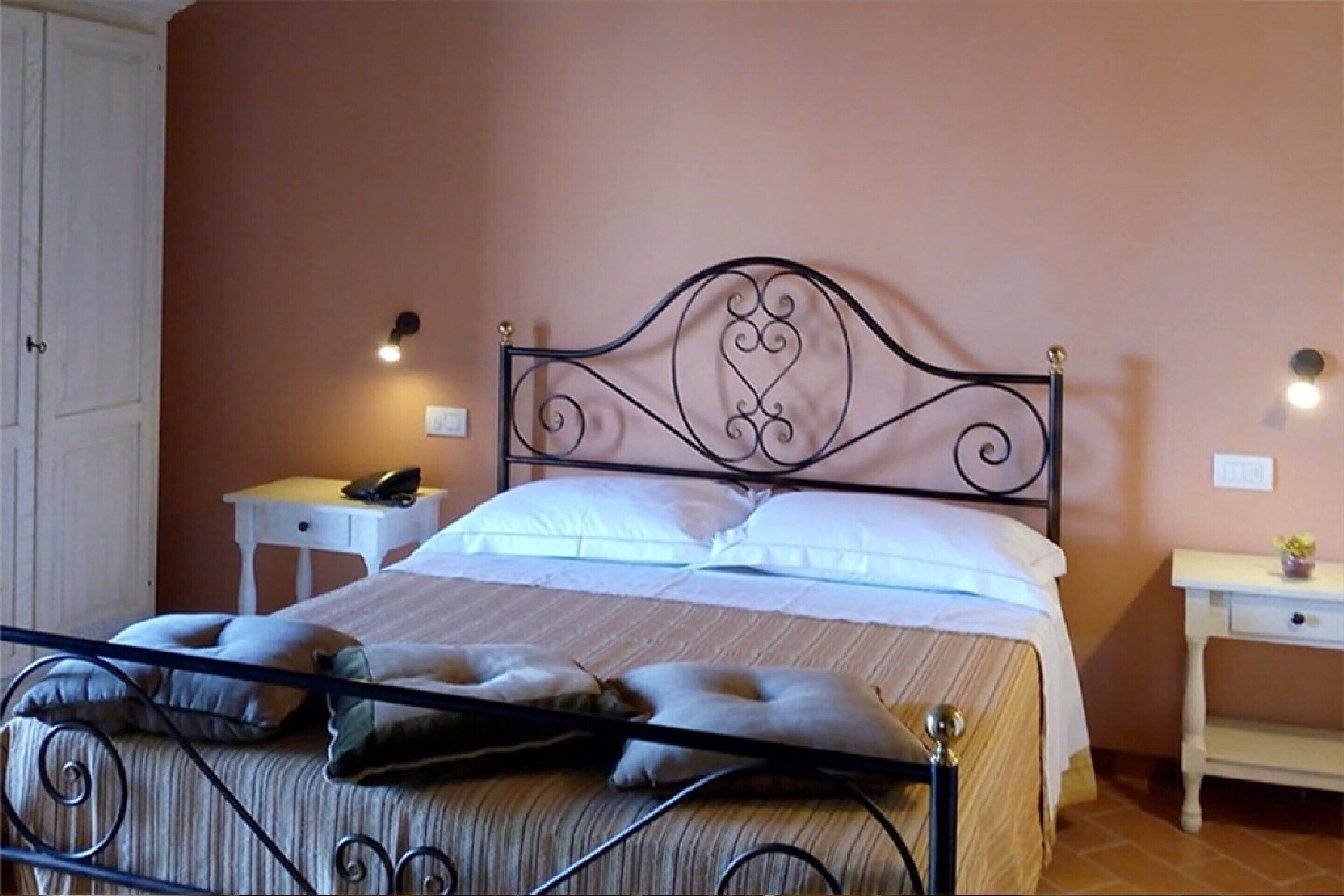 Un lit bien fait, avec une tête de lit en métal, deux tables de chevet avec des lampes et, au fond, une porte blanche.