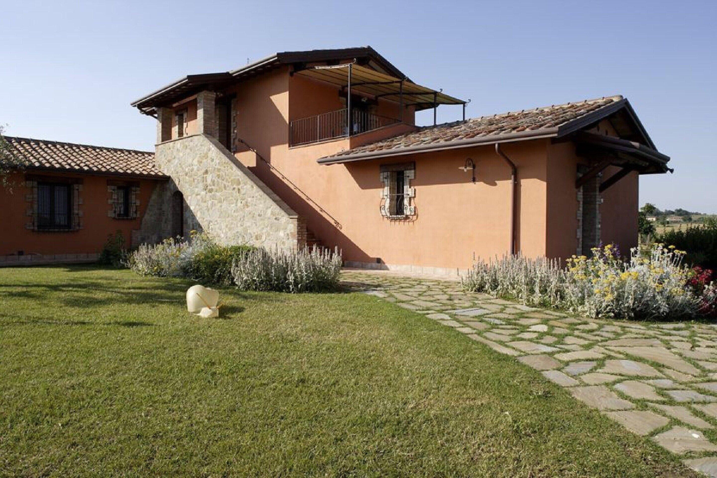 Une maison à deux étages avec un escalier en pierre, un balcon et un jardin aménagé avec une allée pavée.
