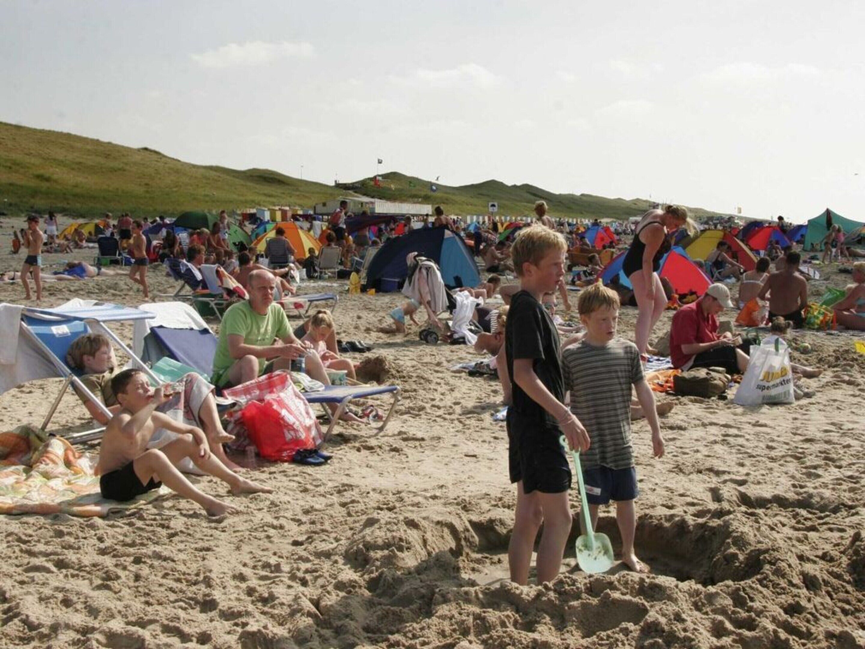 A crowded beach with people sitting on chairs and tents in the background.