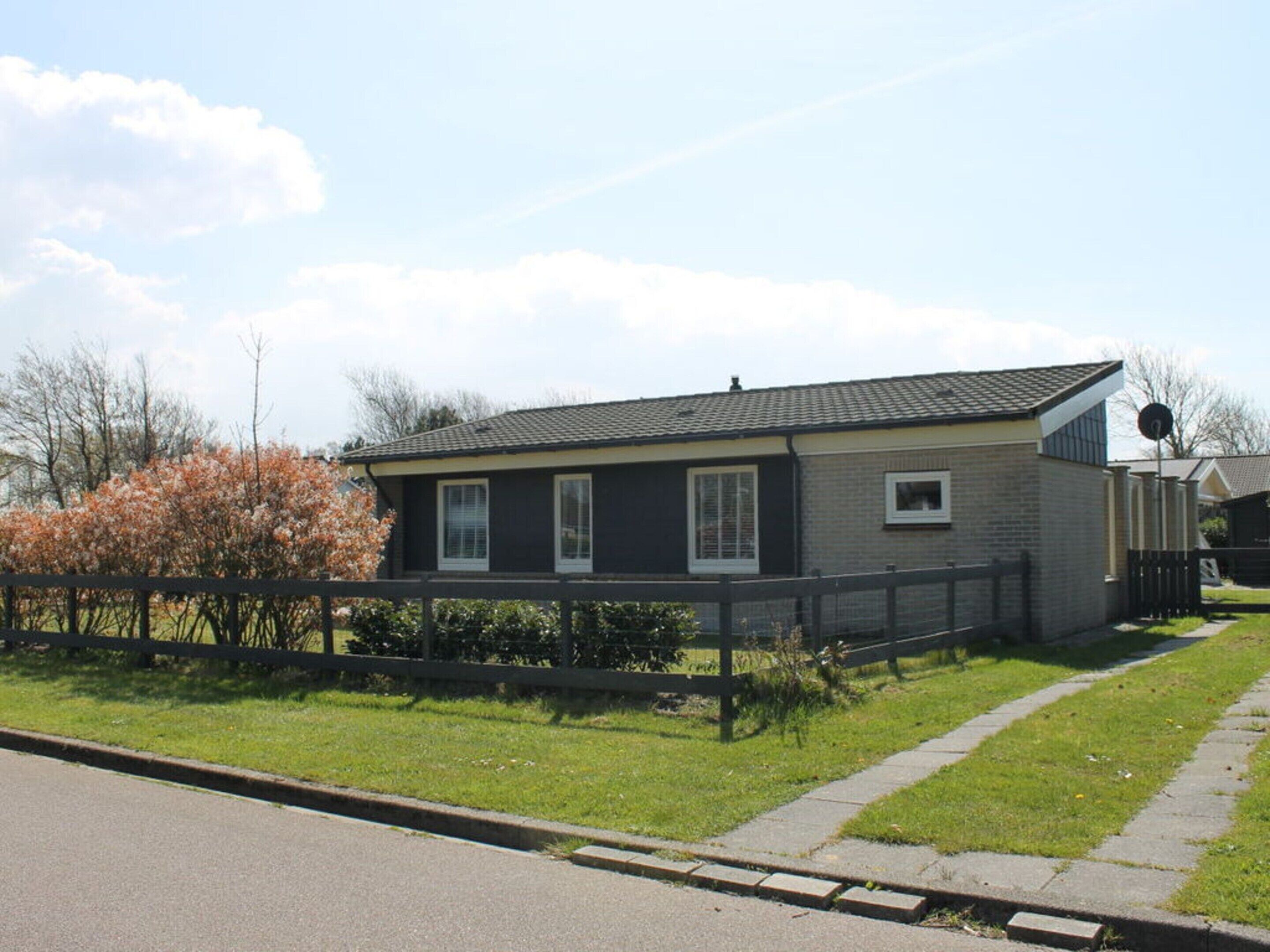 A single-story house with a dark exterior, a sloped roof, and a satellite dish on the roof.