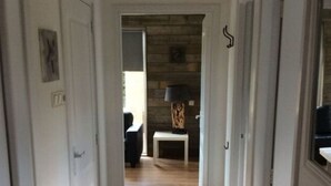 A hallway with wooden flooring leading to a room with a stone wall and a lamp on a small table. - Lovely Apartment in Julianadorp (Julianadorp)