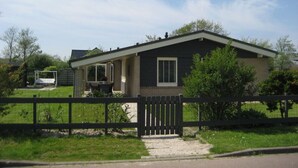 A single-story house with a dark roof, a front porch, and a fenced backyard. - Lovely Apartment in Julianadorp (Julianadorp)