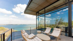 Ein moderner Außenbereich zum Sitzen mit Korlounge-Stühlen und einem runden Tisch, mit Blick auf ein malerisches Gewässer und Grünflächen.