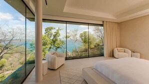 Ein modernes Schlafzimmer mit einem großen Bett, einer Sitzecke und Blick auf eine natürliche Landschaft.
