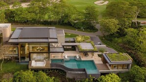 Ein modernes Haus mit Swimmingpool, großen Glasfenstern und Blick auf einen Golfplatz.