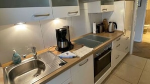 Eine kleine Küche mit weißen Schränken, einem Edelstahl-Spülbecken, einer Kaffeemaschine und einer Mikrowelle.