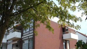 Ein mehrstöckiges Gebäude mit Ziegelaußenwand, Balkonen und einem Baum im Vordergrund.