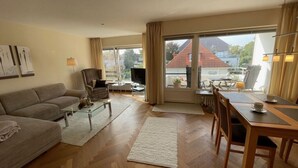 Ein geräumiges Wohnzimmer mit einer Couch, einem Couchtisch, einem Fernseher und einem Essbereich mit Tisch und Stühlen.
