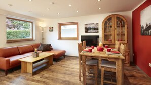 A cozy living room with a sofa, a wooden coffee table, and a dining table set for four. - Holiday Apartment in Bavaria (Schoenau am Koenigssee)