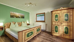 A bedroom with a wooden bed, a green wall, a wooden wardrobe, and a window with a view of greenery. - Holiday Apartment in Bavaria (Schoenau am Koenigssee)