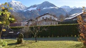 A rustic building with a sloped roof, surrounded by a well-maintained garden and a view of snow-capped mountains. - Holiday Apartment in Bavaria (Schoenau am Koenigssee)