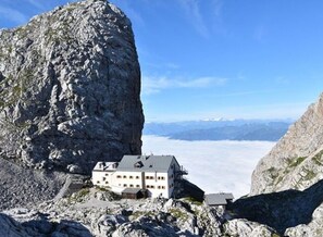 A mountain lodge with a large rock formation nearby, offering a view of distant mountains. - Holiday Apartment in Bavaria (Schoenau am Koenigssee)