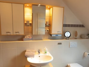 A bathroom with a sink, mirror, towel rack, and a small shelf with decorative items.
