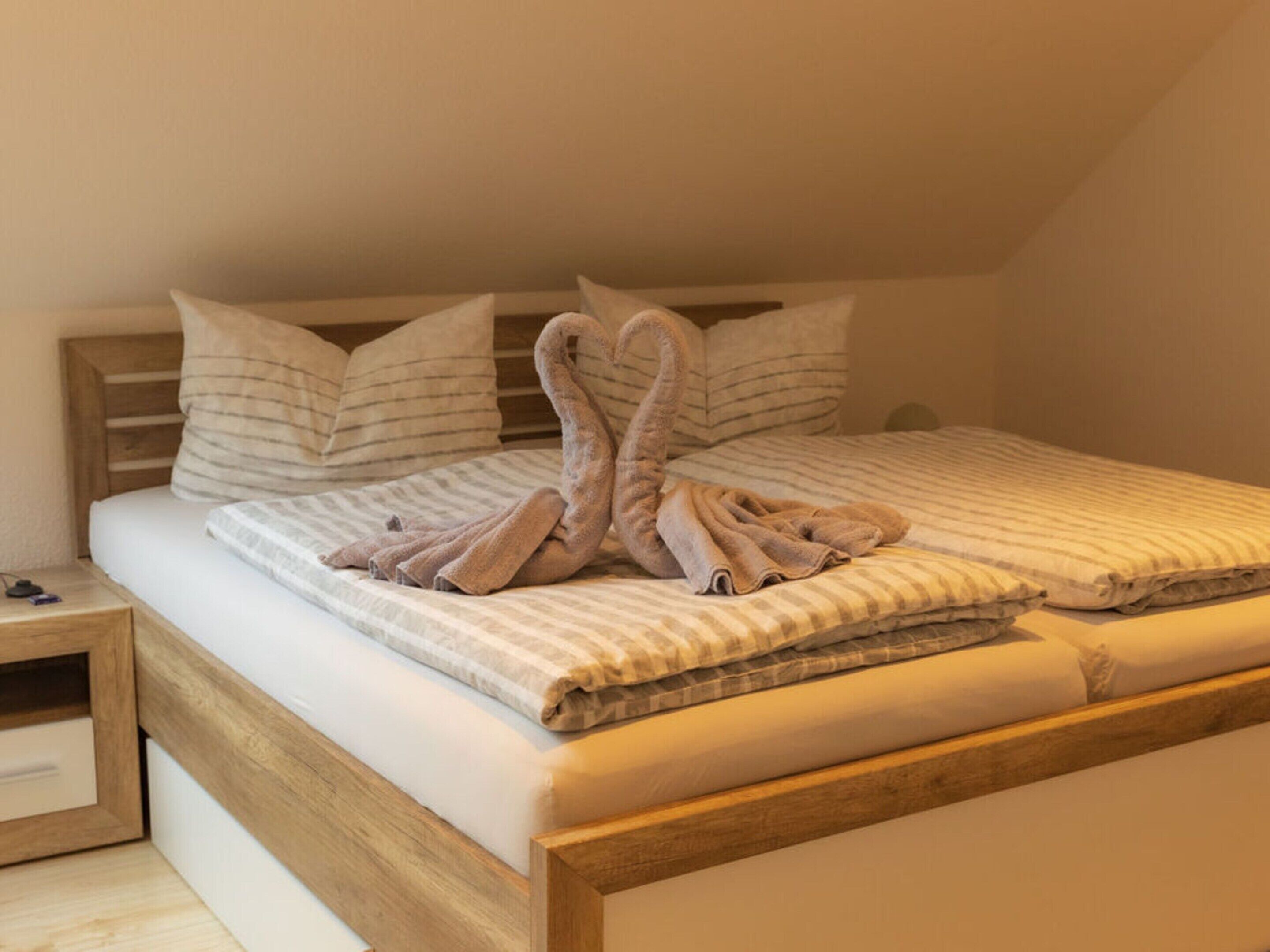 Una cama bien hecha con ropa de cama a rayas y dos almohadas, un cabecero de madera y una mesita de noche con una lámpara.