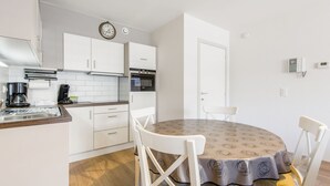 A compact kitchen with white cabinets, a built-in oven, a coffee maker, and a dining table with four chairs. - Apartment Near the Grand Place (Blankenberge)