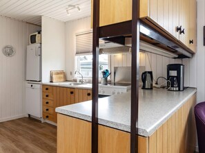 A kitchen with wooden cabinets, a countertop, a microwave, a coffee maker, and a window with blinds. - 7 Person Holiday Home in Hals (Hals)