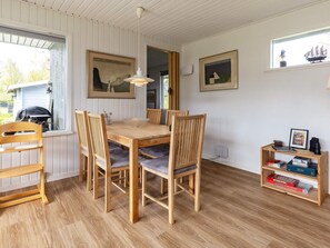 A dining area with a wooden table and chairs, a hanging light fixture, and a bookshelf with books and games. - 7 Person Holiday Home in Hals (Hals)