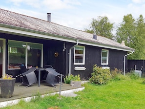 Ein Haus mit überdachter Terrasse, einem Esstisch mit Stühlen und einem kleinen Garten.