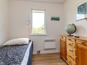 A bedroom with a bed, a window, a radiator, a wooden dresser, and a globe.