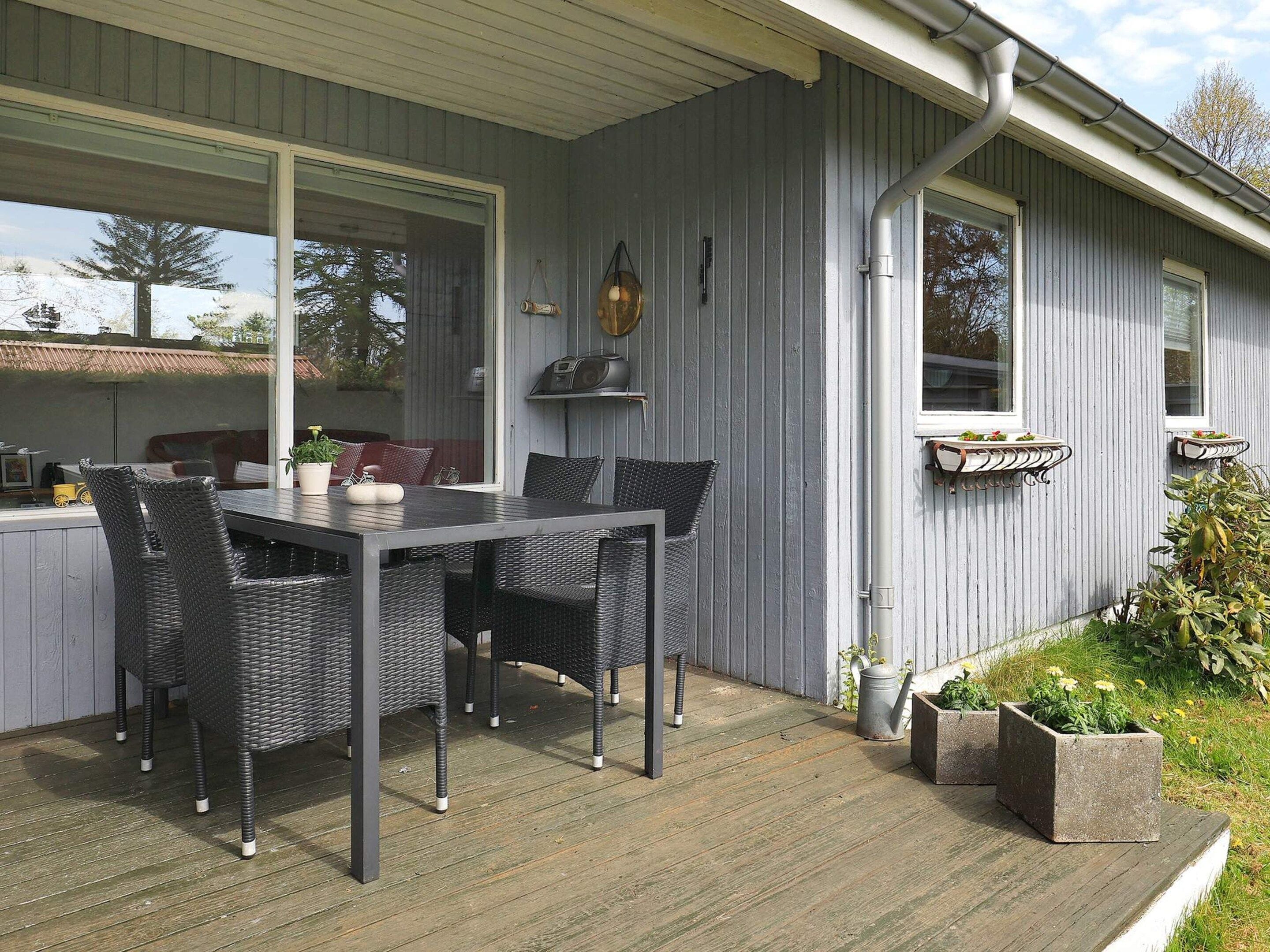 A covered patio with a dining table and chairs, a radio, and potted plants.