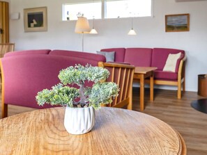 A room with a round wooden table in the foreground, a red sofa, a wooden chair, and a small potted plant. - 7 Person Holiday Home in Hals (Hals)