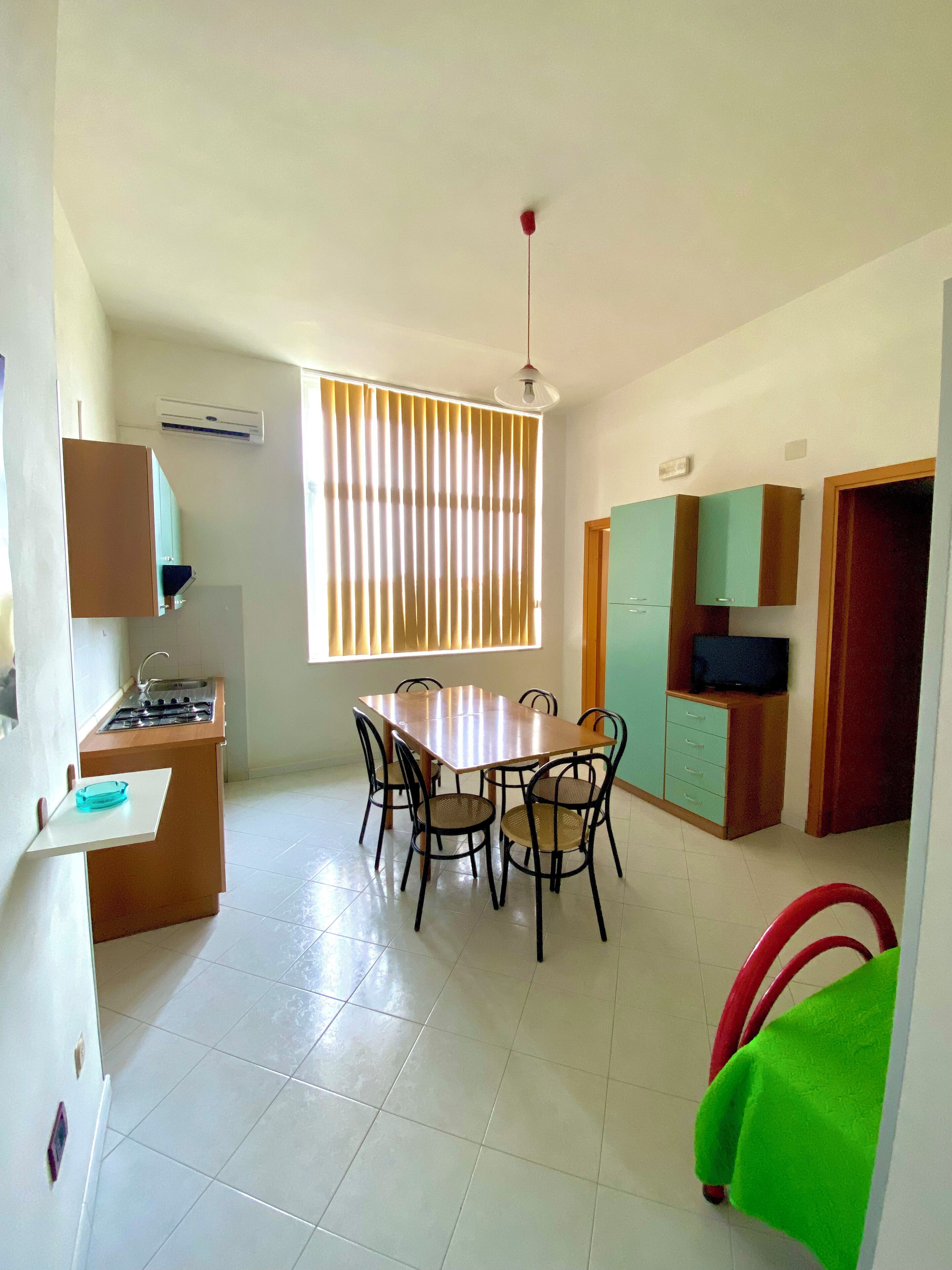 A compact kitchen with a dining table, chairs, a stove, and a window with blinds.