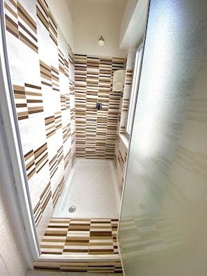 A narrow shower area with a sloped floor and a wall with a striped pattern. - Residence Felix (Ricadi)