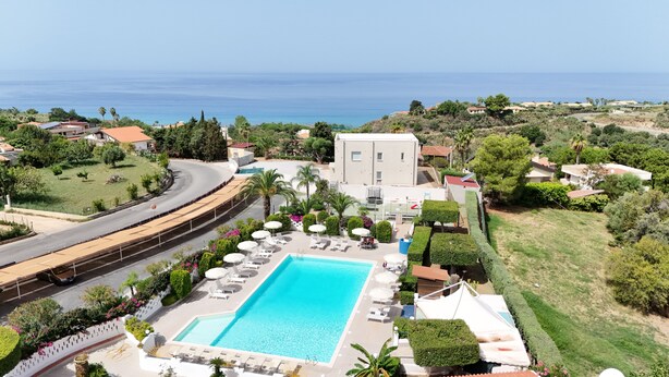 A resort with a swimming pool, lounge chairs, and a view of the sea. - Residence Felix (Ricadi)