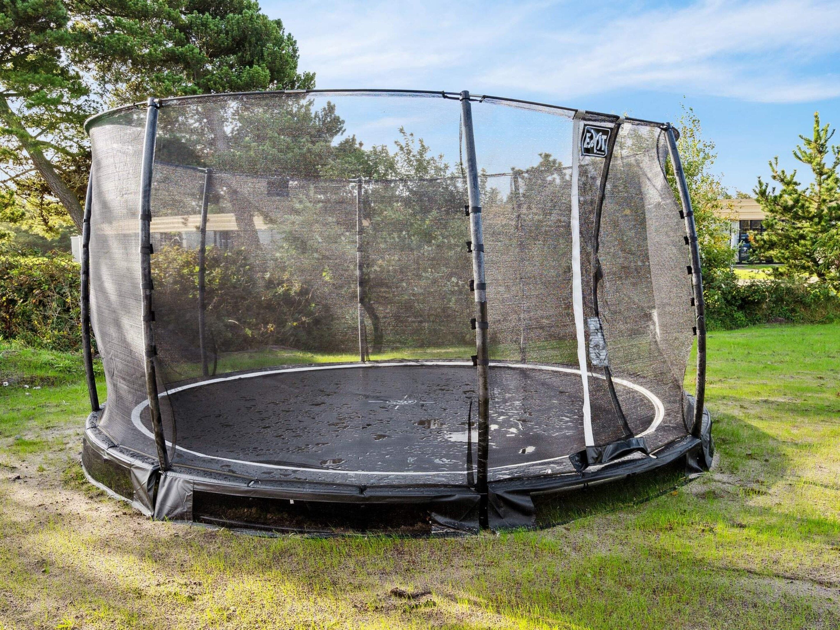 A circular trampoline with a safety net enclosure, surrounded by grass and trees.