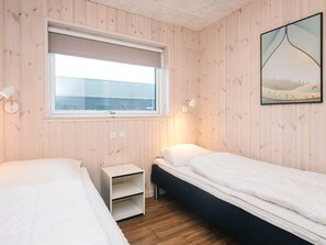 A bedroom with two beds, a window, a bedside table, and a wall-mounted lamp.
