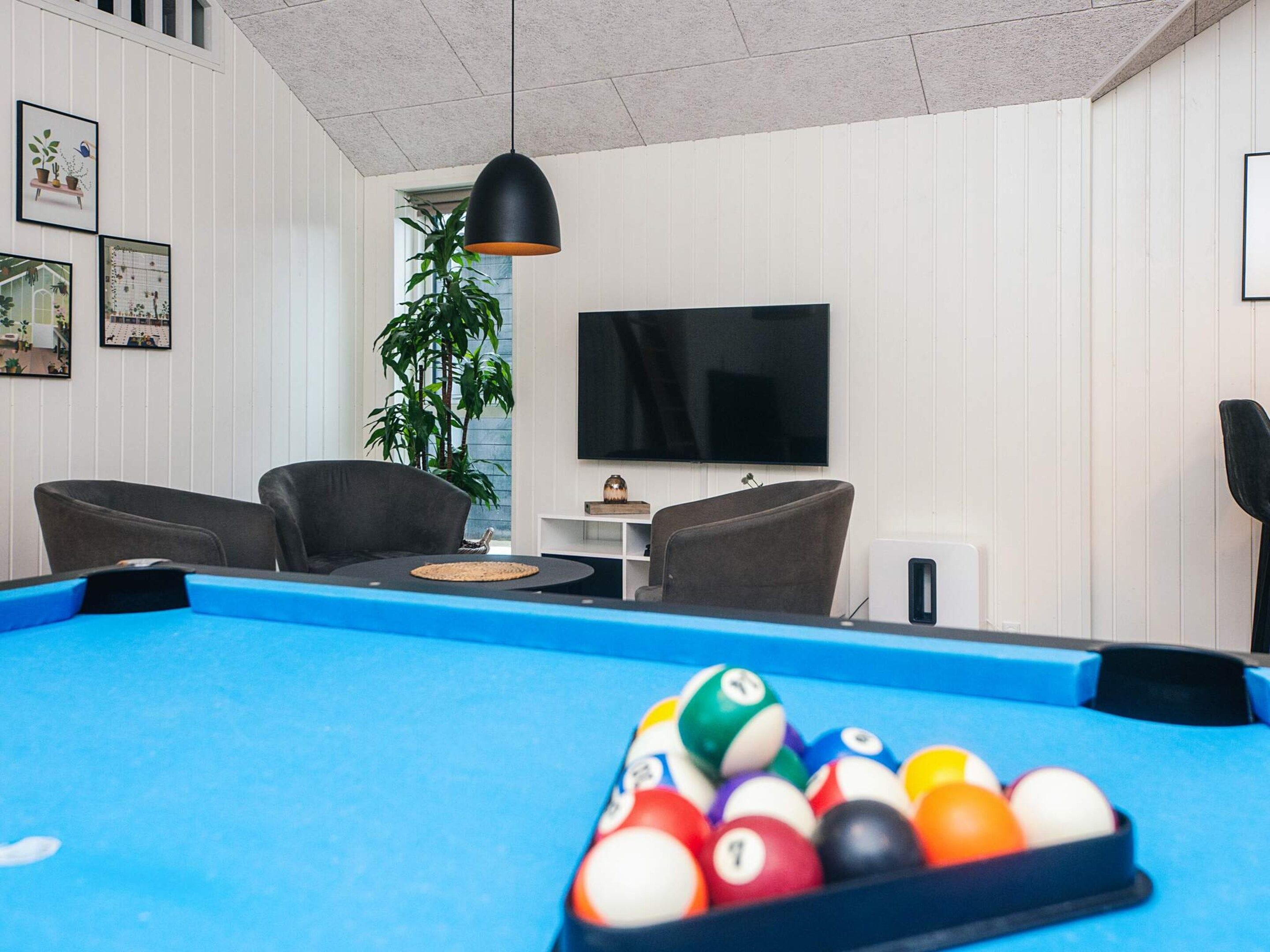 A pool table with balls, two armchairs, a television, and framed pictures on the wall.