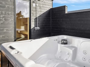 A hot tub with a wooden deck and a black wall in the background.