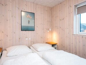 Ein Schlafzimmer mit zwei Einzelbetten, einer Holzvertäfelung, einem gerahmten Bild, einem Nachttisch mit Lampe und einem Fenster.