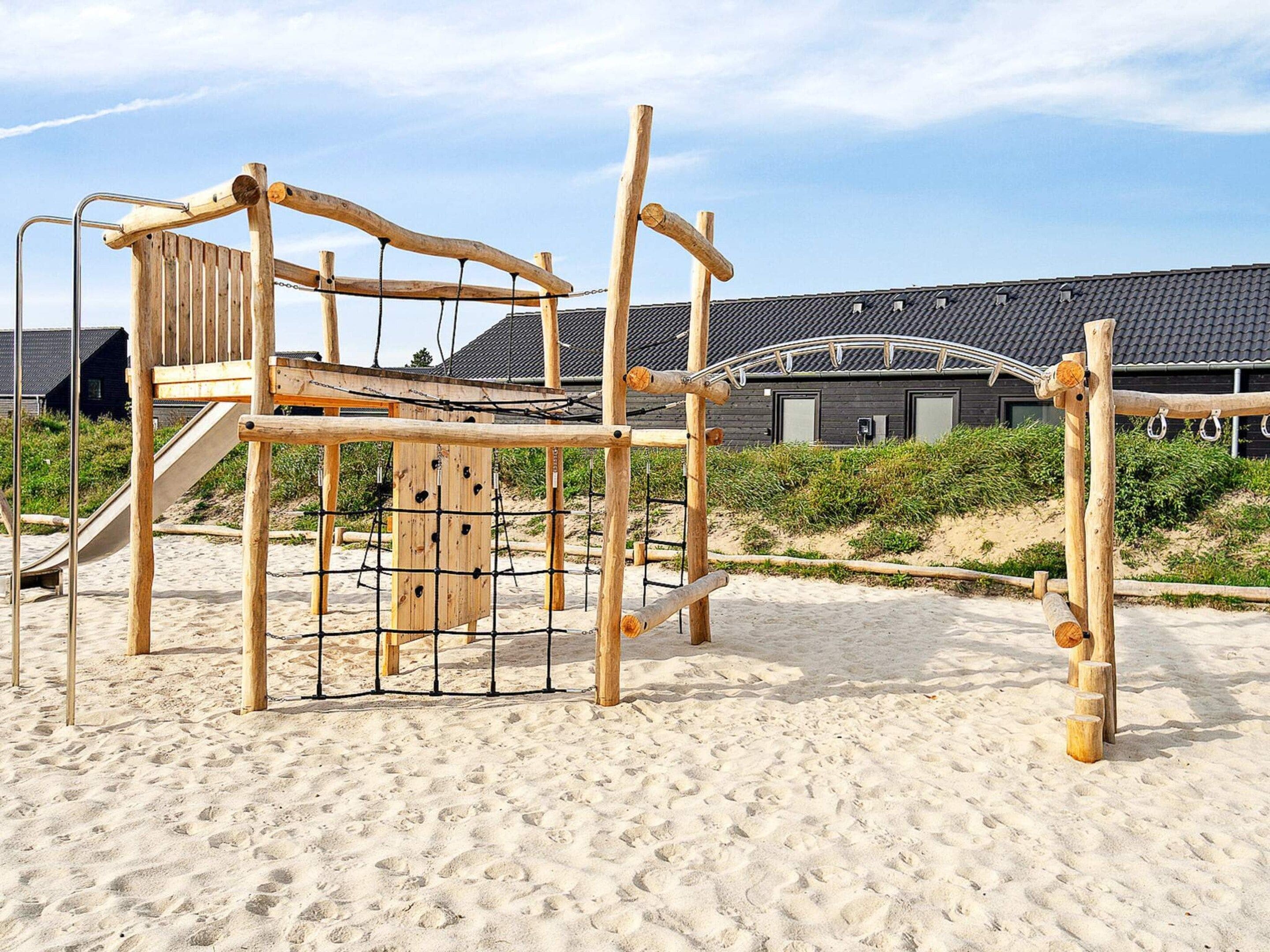 A wooden play structure on a sandy beach with a building in the background.
