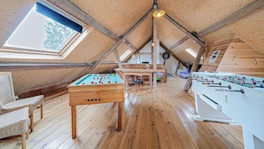Une pièce au plancher de bois, équipée d’un baby-foot, d’une table de billard et d’une table de ping-pong.