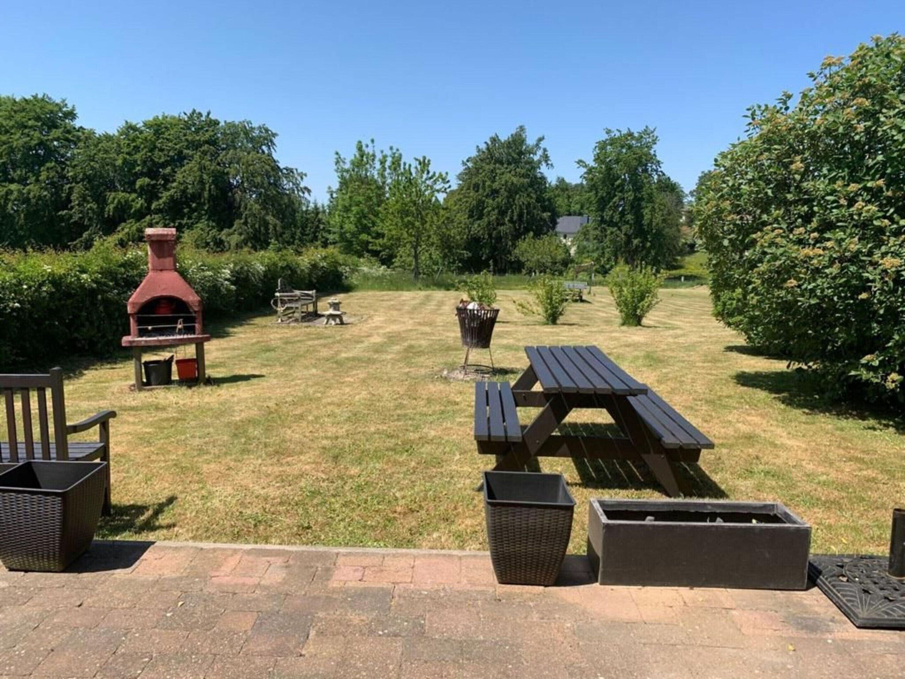 A backyard with a barbecue grill, picnic table, chairs, and a trash bin.