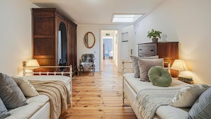 Une pièce avec un plancher en bois, un lit doté d’une tête de lit blanche, un canapé, une chaise, un miroir, une armoire et une petite table avec une lampe.